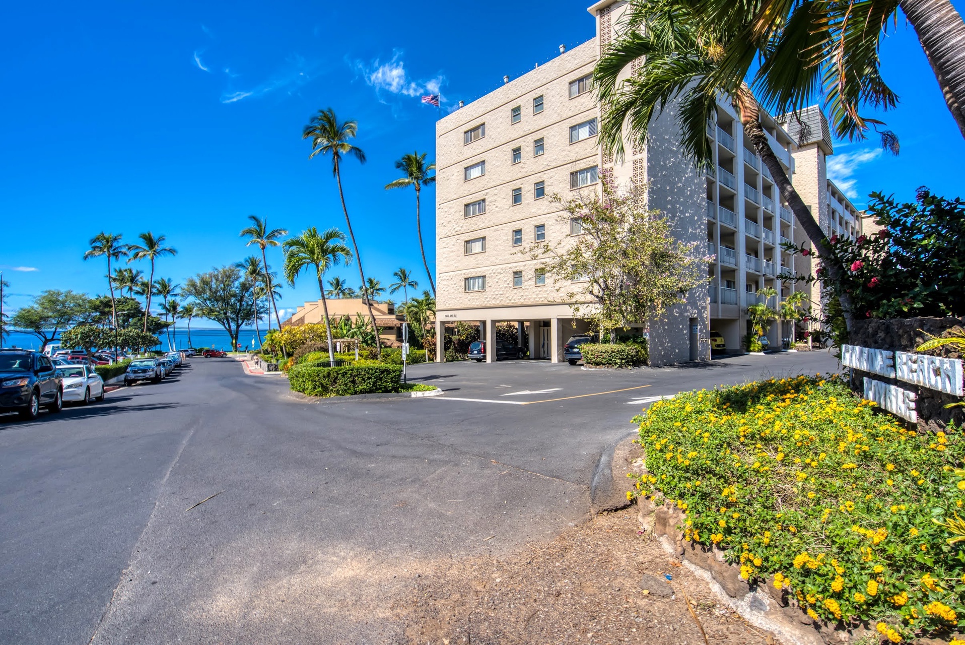 A tropical beachfront property featuring convenient parking and lush landscaping with swaying palms, located steps from the ocean in a tranquil coastal setting.