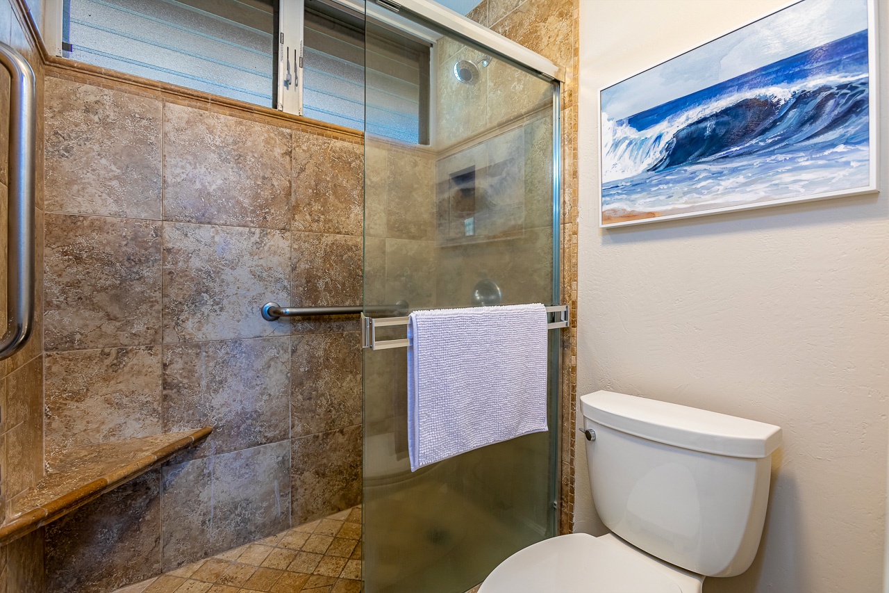 Refresh in your private bathroom featuring a spacious walk-in shower with beautiful stone tile, fluffy towels, and coastal artwork to set a serene mood.