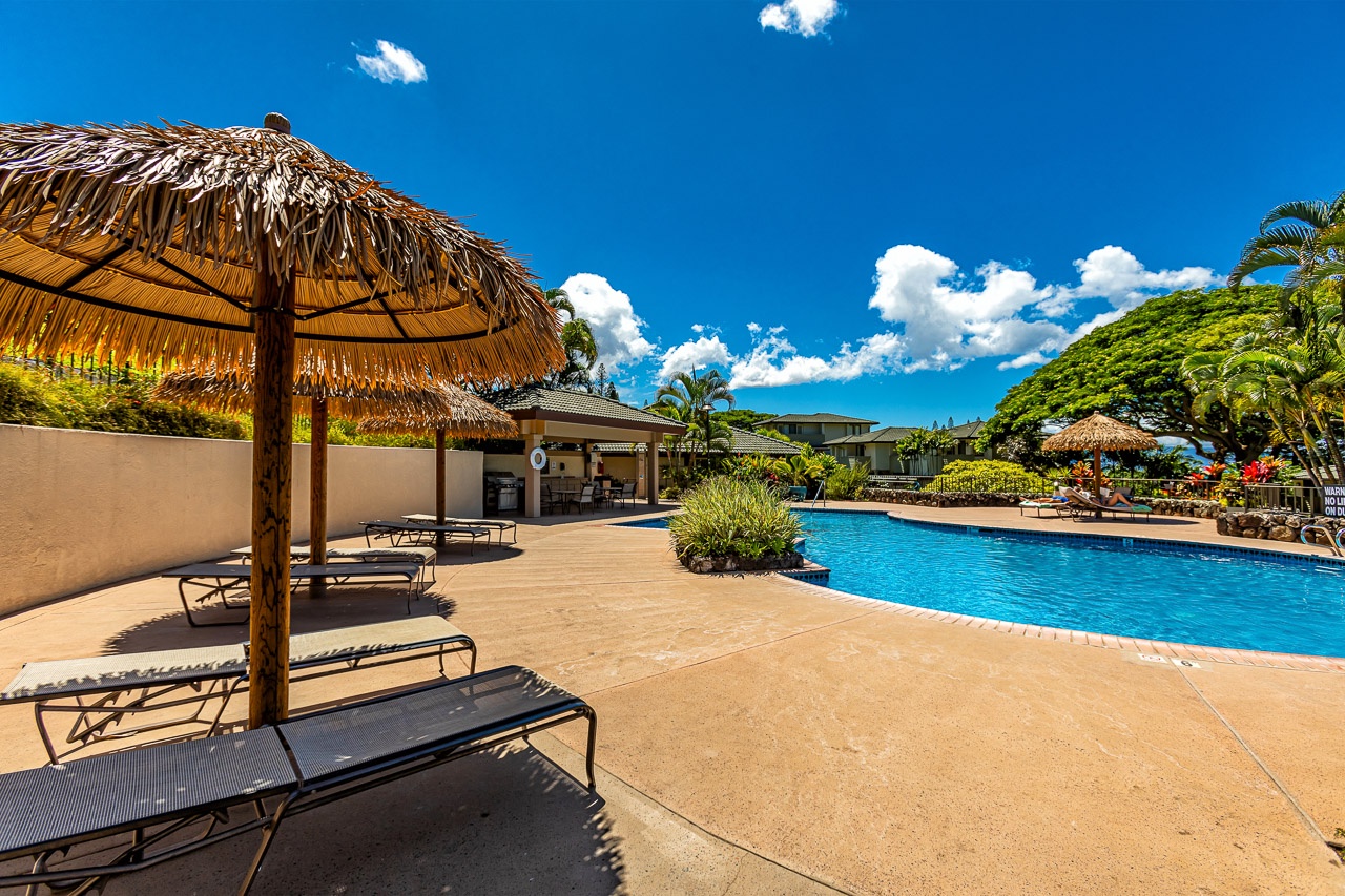 A sparkling pool awaits under brilliant blue skies, framed by swaying palms and a shaded tiki hut—your perfect spot to unwind in paradise.