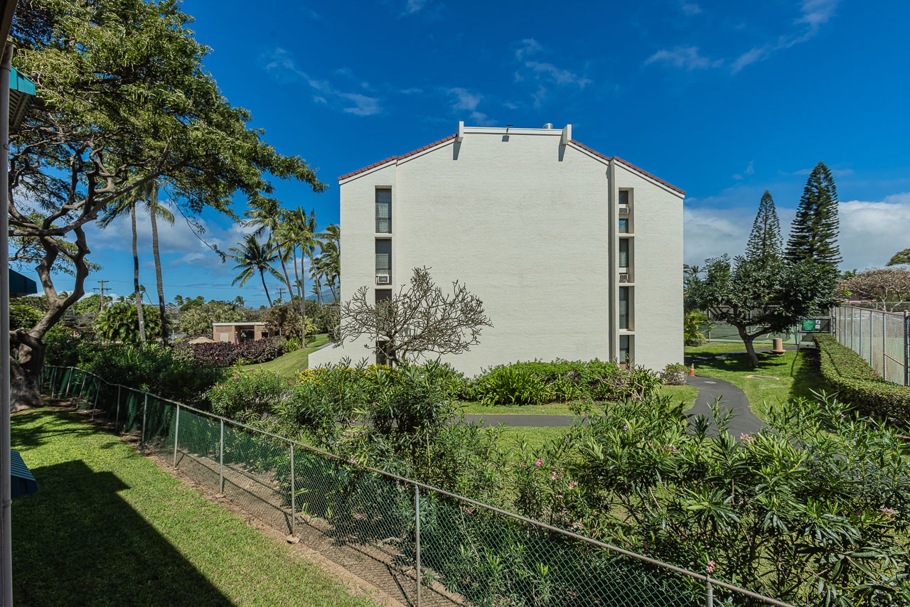 Modern beachside building surrounded by tropical gardens and towering palms under brilliant blue Hawaiian skies.