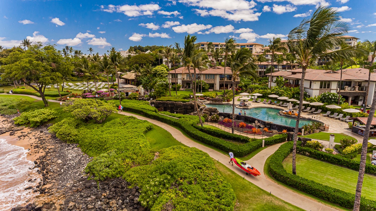 This stunning aerial view showcases the property's oceanfront location, lush tropical gardens, winding pathways, and inviting pool area—all set against a pristine shoreline and vibrant blue skies.