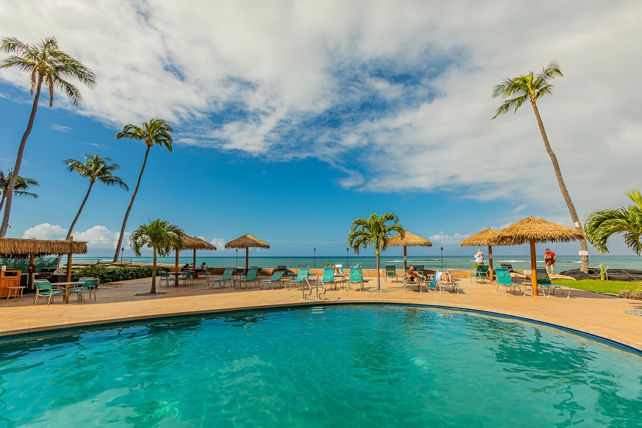 The beachside pool opens to turquoise waters and swaying palms, with thatched umbrellas and lounge chairs dotting the shoreline.
