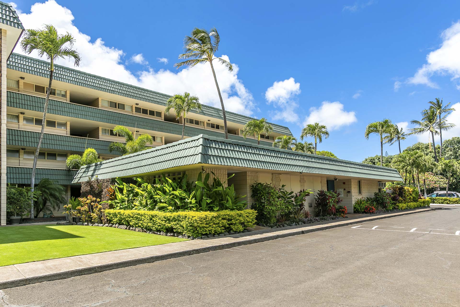 A tropical resort entrance surrounded by swaying palm trees, lush gardens, and manicured lawns under a brilliant blue Hawaiian sky.