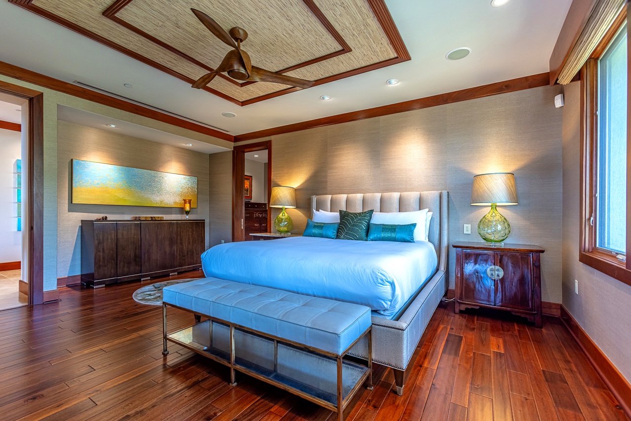Unwind in this elegantly designed bedroom with rich wood floors, coffered ceiling, and plush bedding accented in turquoise. Soft lighting creates the perfect mood for a restful night.
