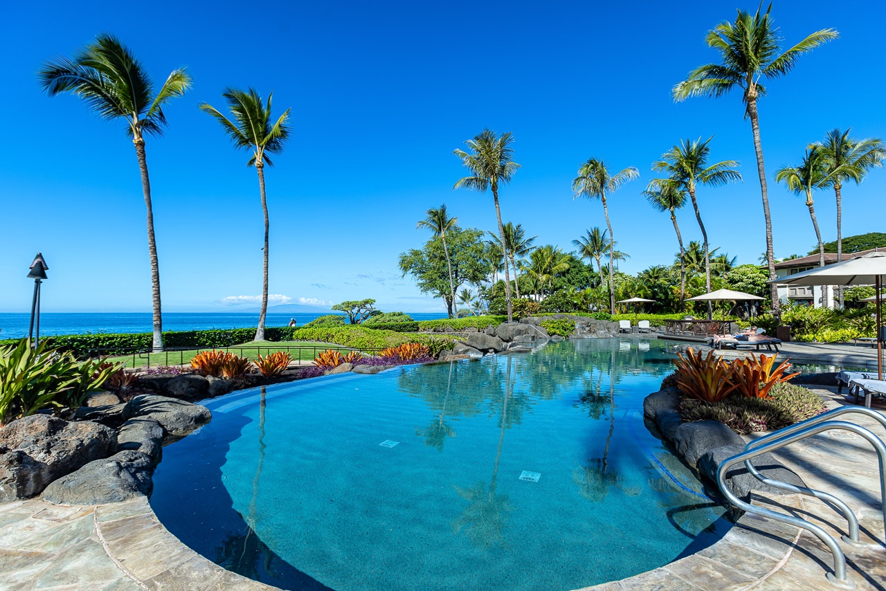 Stunning resort-style pool set against swaying palms and sparkling ocean waters, where tropical breezes and endless blue skies create your perfect island escape.