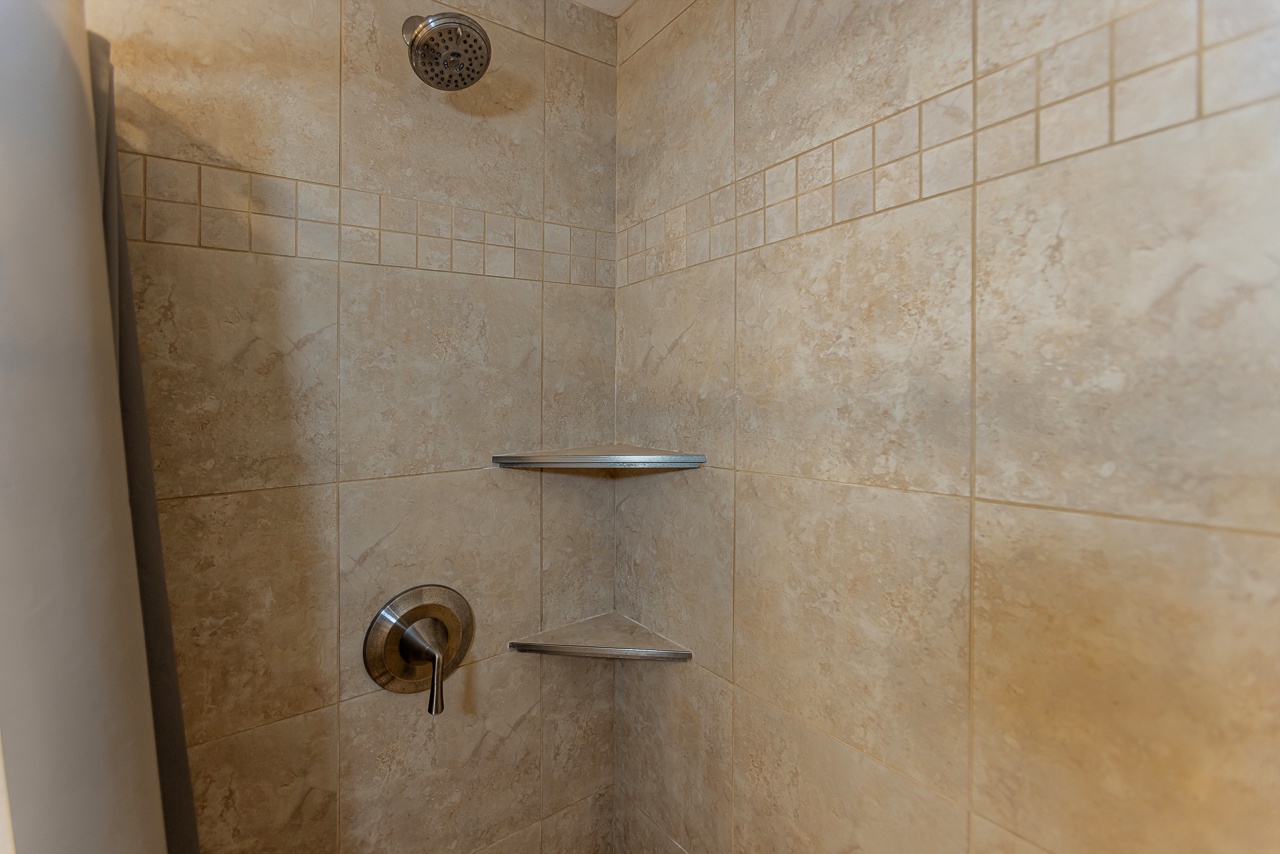 Step into your private shower with warm beige tile, built-in corner shelves for your essentials, and a rainfall showerhead to start your day refreshed.