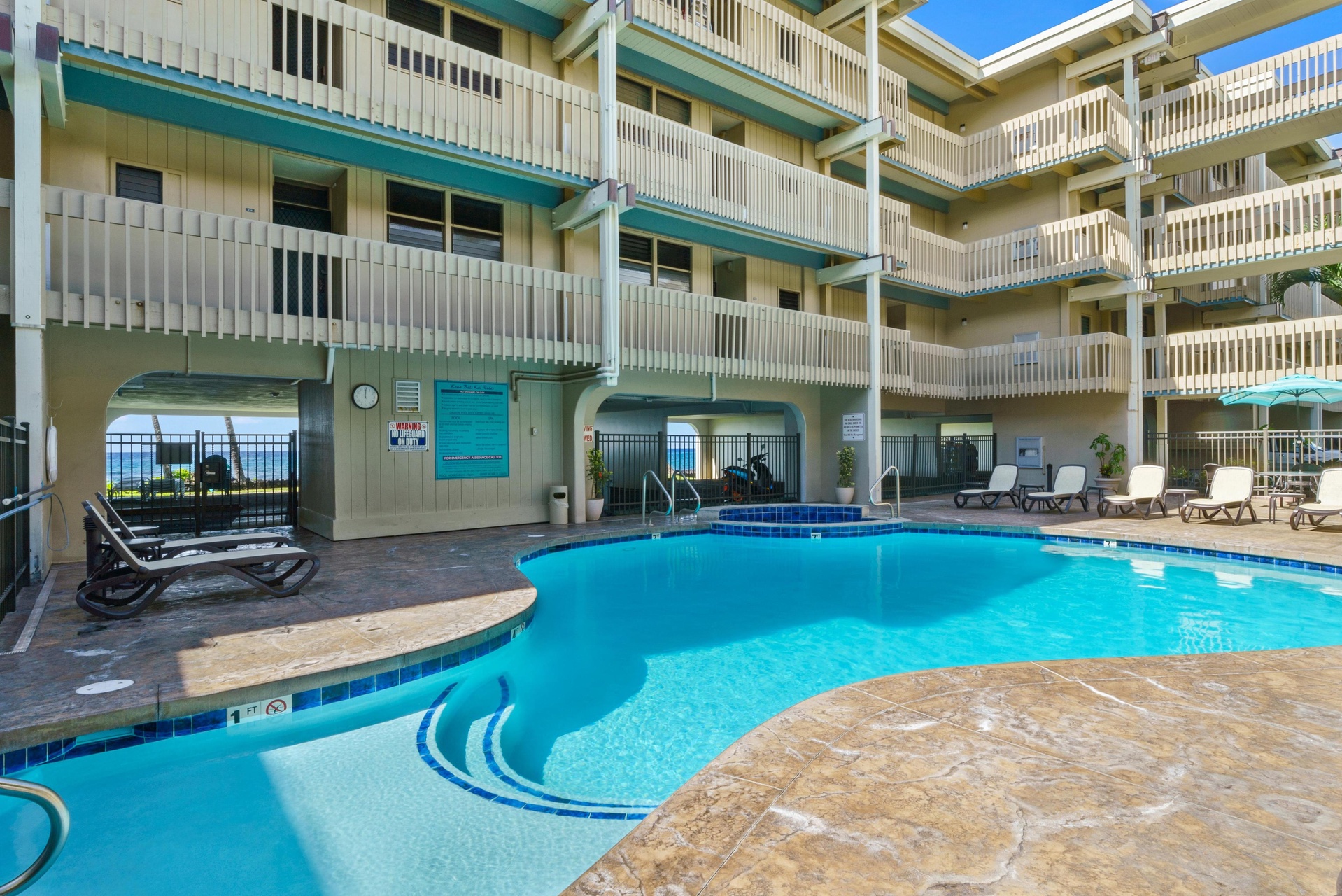 The property features a central courtyard pool surrounded by multiple floors of guest rooms with private balconies, creating a relaxed beachside atmosphere.