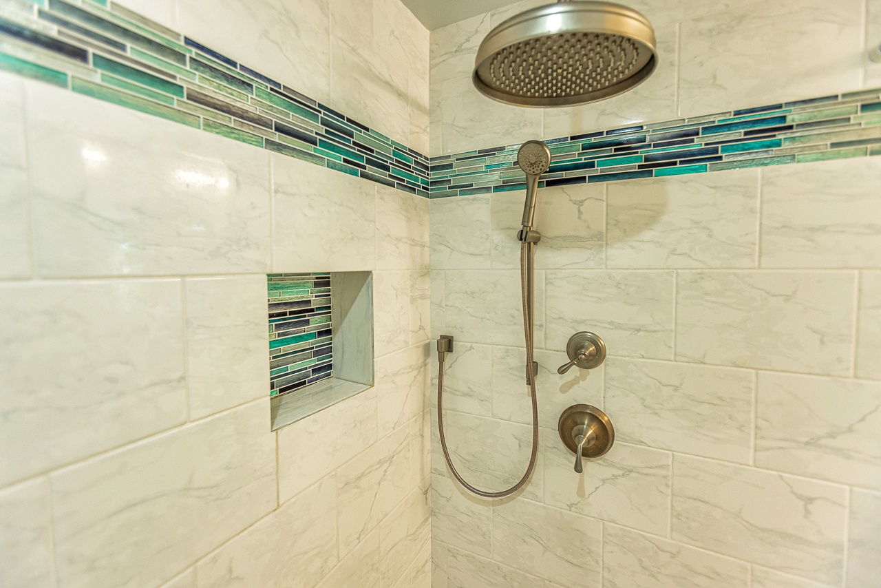 Step into your private spa-like shower with dual rainfall and handheld options, elegant marble tile, and a soothing glass mosaic accent—pure relaxation awaits.