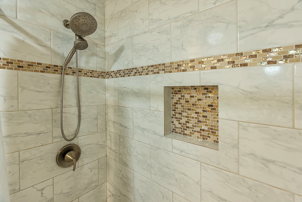 Luxurious marble-tiled walk-in shower with dual showerheads, bronze fixtures, and mosaic accent tile—your private spa-like retreat awaits.