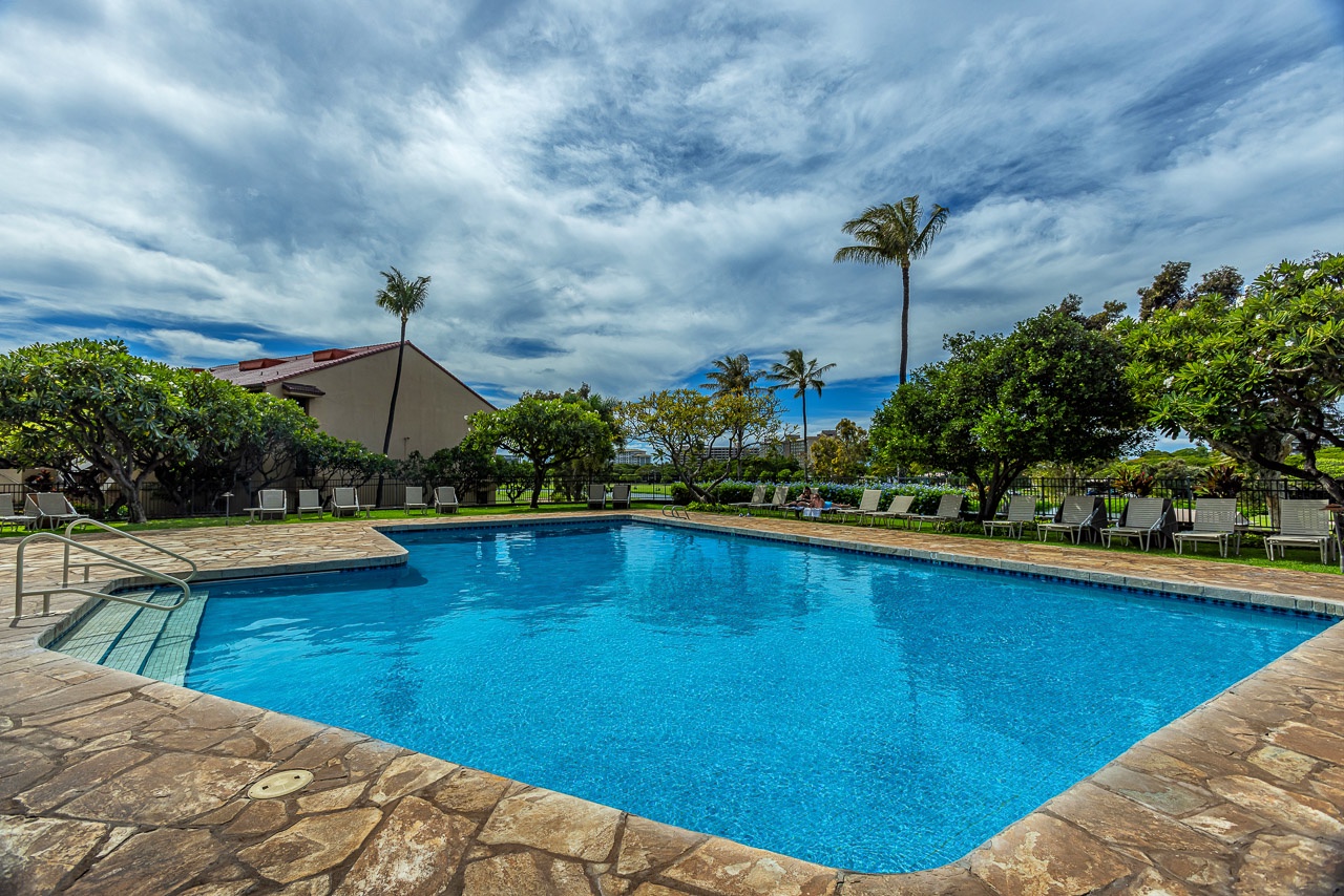 The pristine pool area framed by towering palms and lush tropical landscaping, with the manicured golf course stretching beyond.