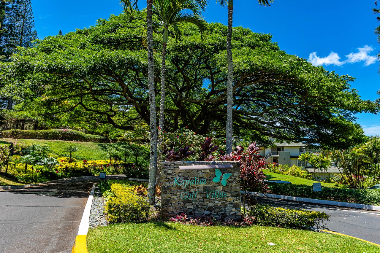 A tropical entrance sign marks the property amid lush greenery, majestic shade trees, and landscaped gardens, creating a welcoming arrival experience.