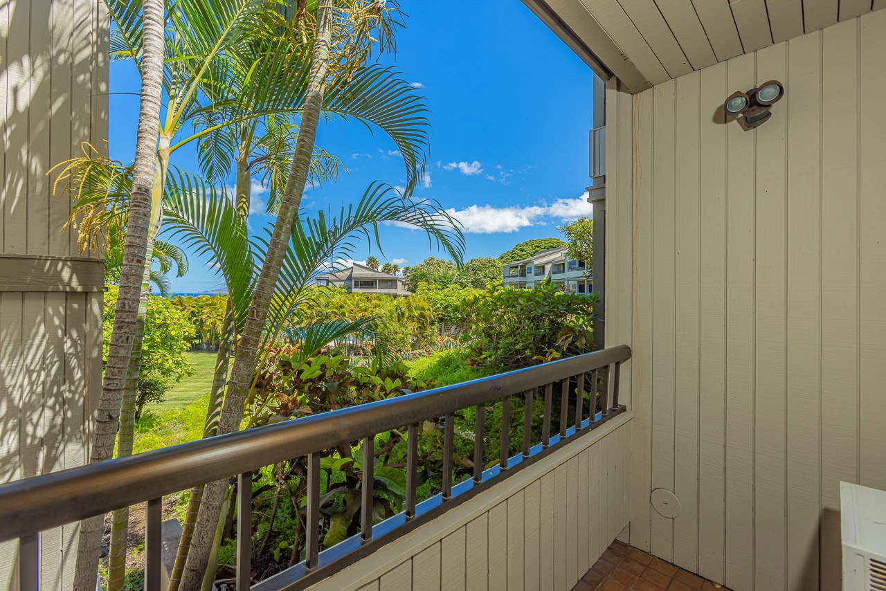 A private balcony framed by tropical palms overlooks lush landscaping and neighboring buildings, offering a serene escape within this sunny resort community.
