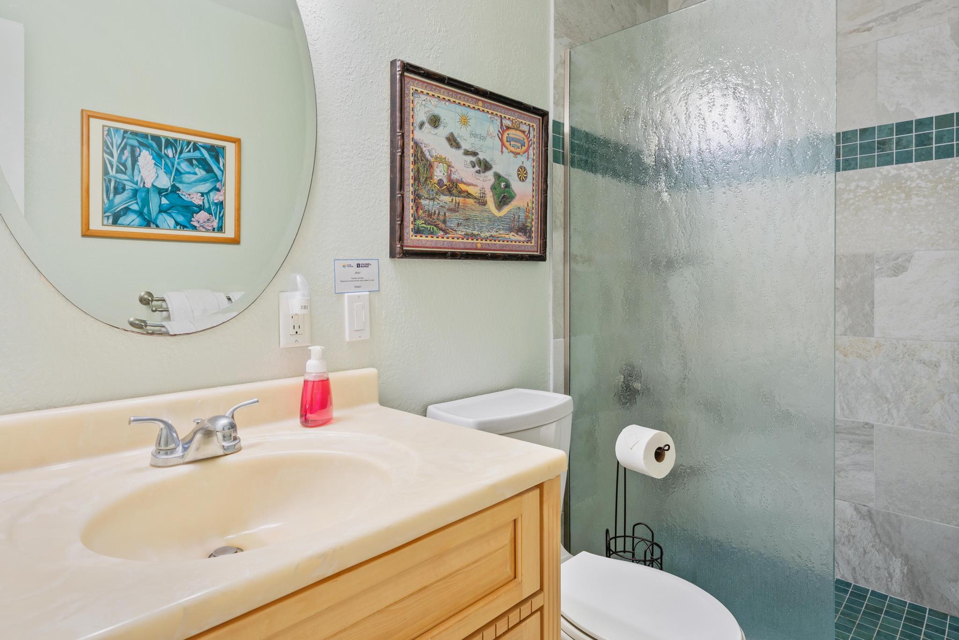 Primary bathroom features a glass-enclosed shower and coastal artwork, creating a fresh, relaxing space to start your day.