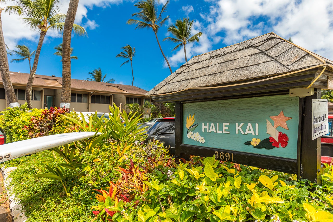 Hale Kai property entrance sign featuring tropical decor and vibrant landscaping beneath swaying palms, marking the start of a peaceful Hawaiian getaway.