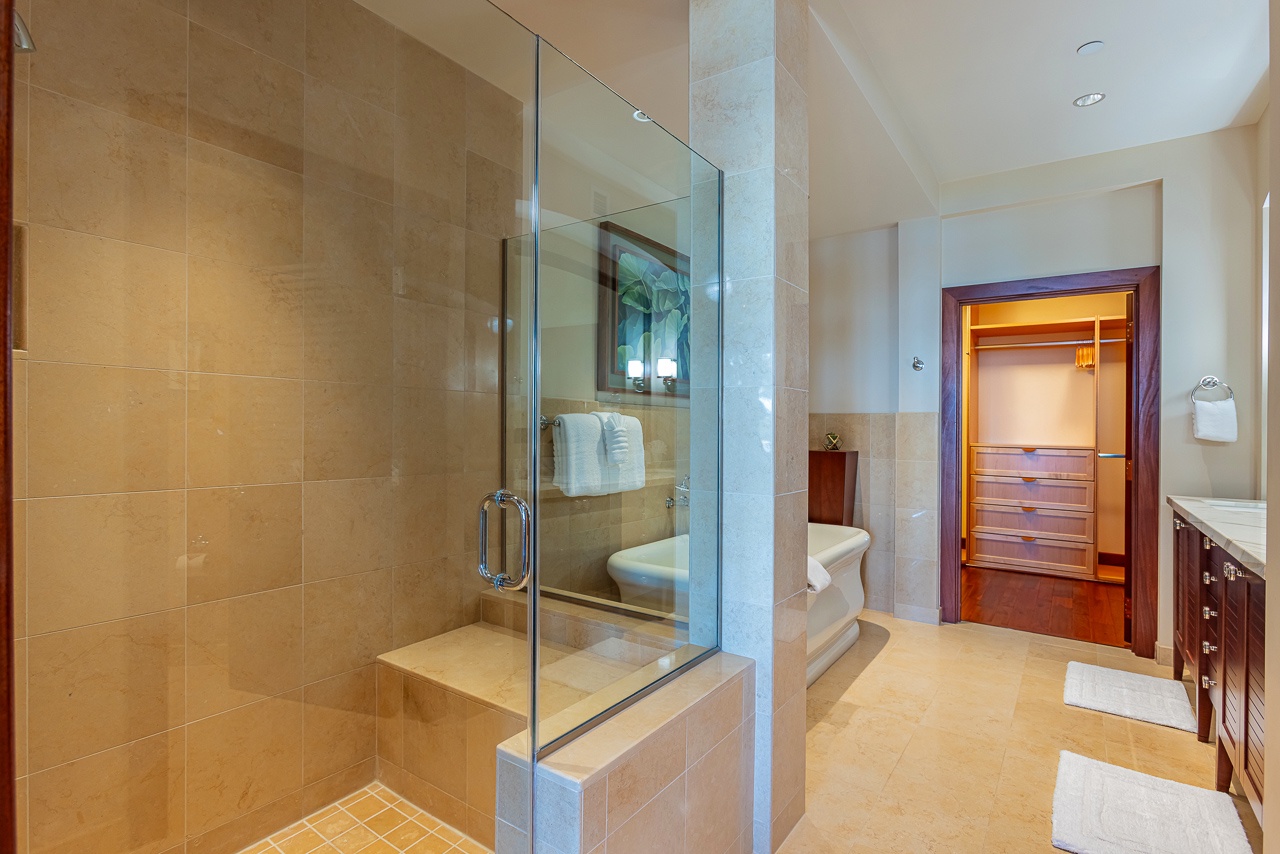 Step into your private spa-like sanctuary, where warm travertine tones and a spacious glass-enclosed shower invite you to unwind.