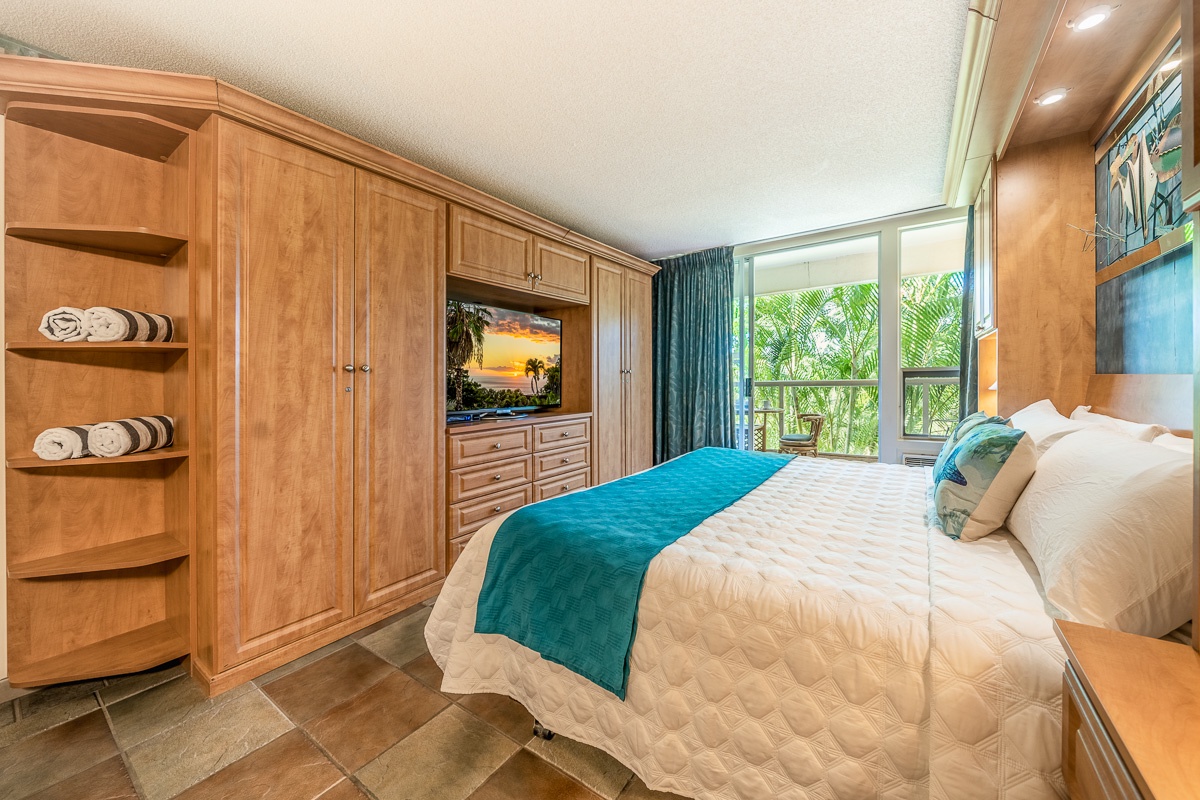 Your inviting bedroom features rich wood cabinetry, a plush bed with tropical accents, and sliding doors opening to a private balcony framed by swaying palms and lush greenery.