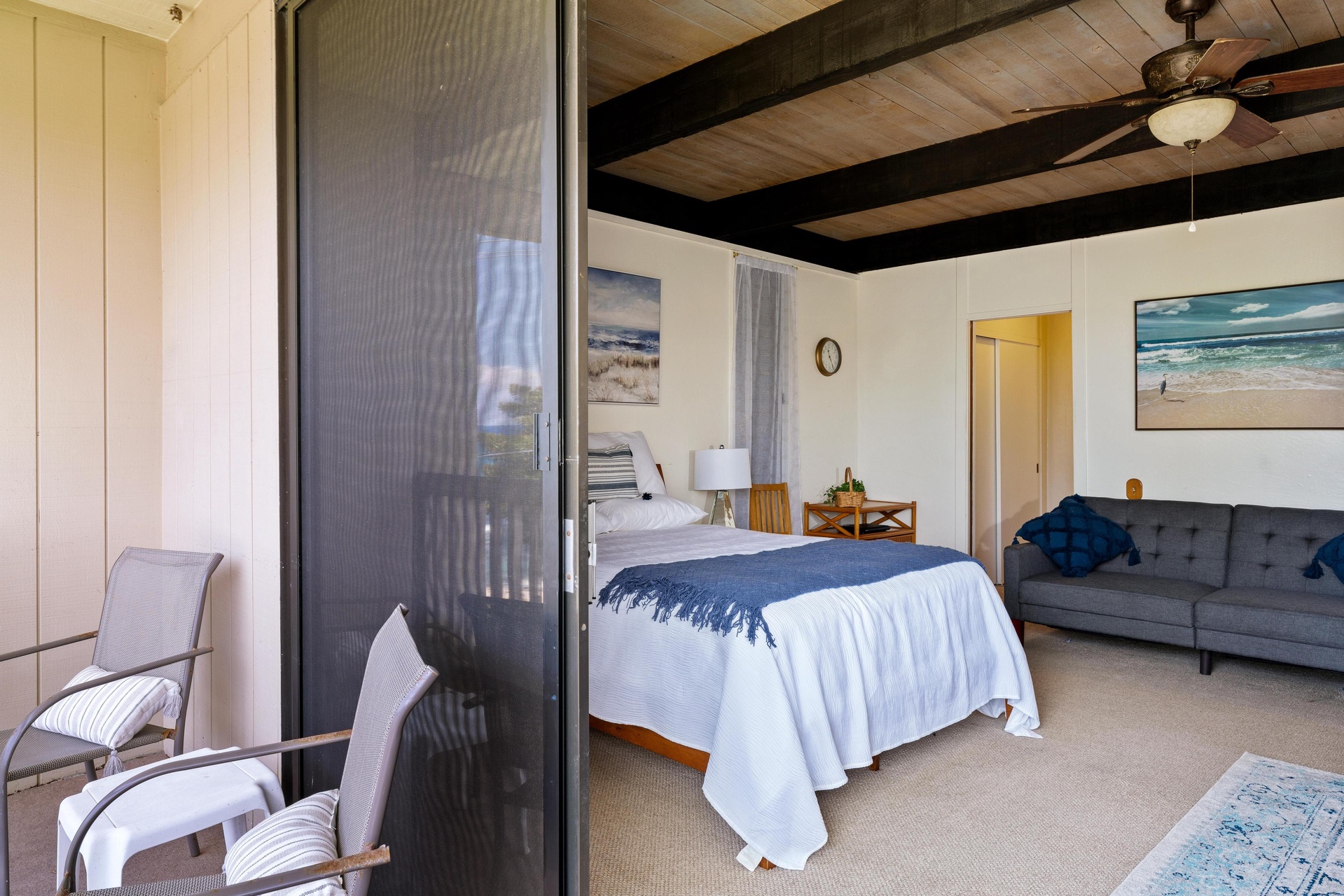 Relax in your coastal-inspired suite with exposed beam ceilings, a plush bed, comfortable sofa, and private balcony where ocean breezes invite peaceful moments overlooking the scenery.