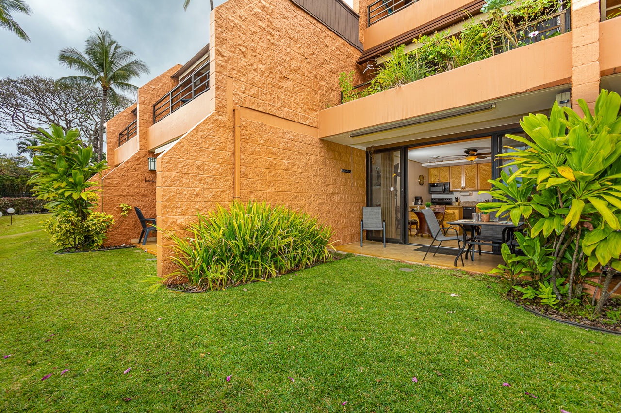 Private ground-floor unit featuring a lush lawn and tropical plantings framed by warm-toned architecture, with dining patio connecting indoor and outdoor spaces.