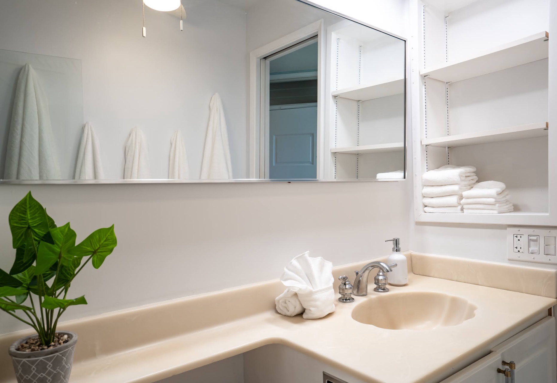 Your private bathroom features a spotless sink, soft towels folded just for you, and open shelving stocked with plush linens—a bright, calming retreat where every detail is ready for your comfort.