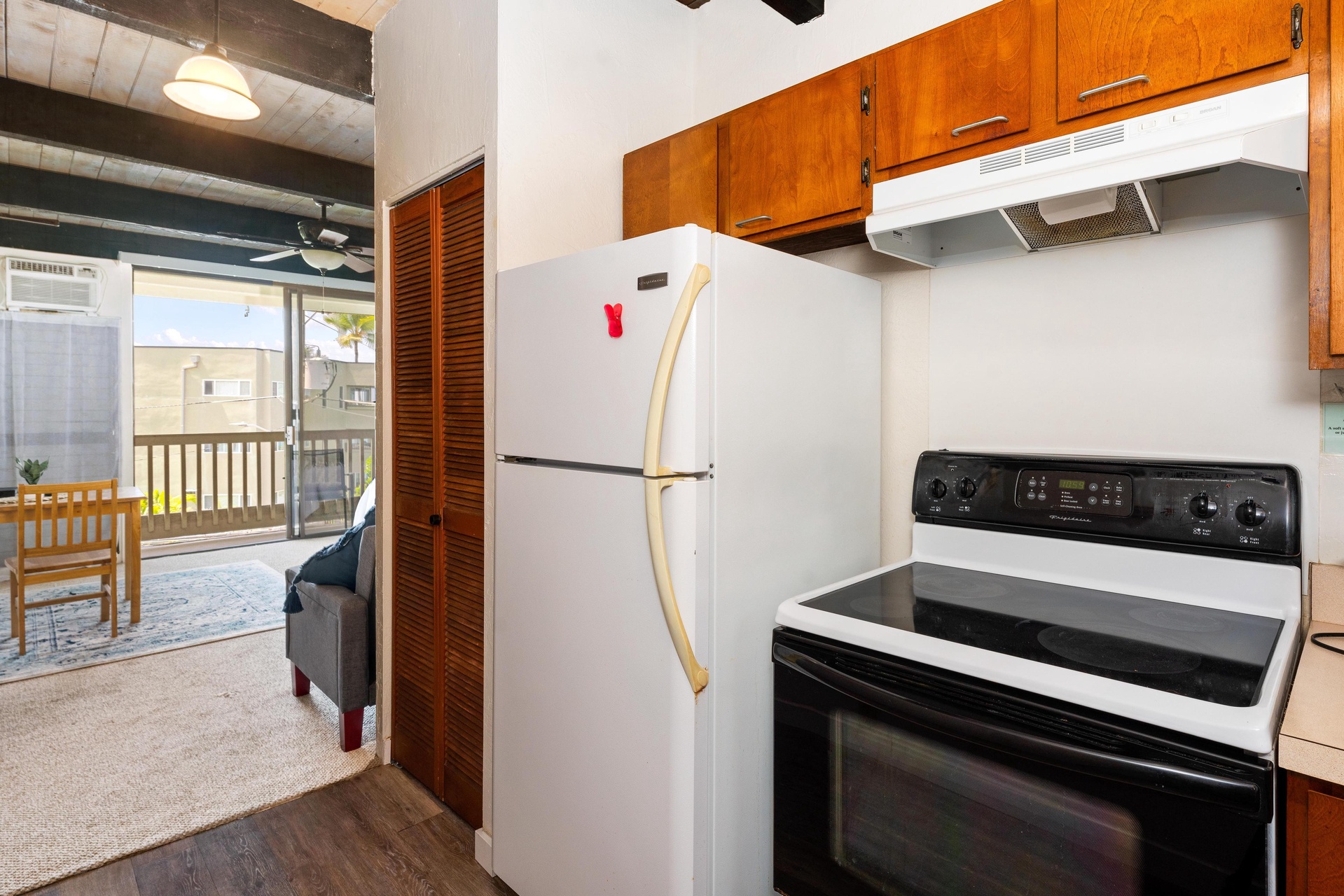 Your well-equipped kitchen features full-size appliances and warm wood cabinetry, opening to a cozy living space with direct balcony access perfect for morning coffee or evening relaxation.