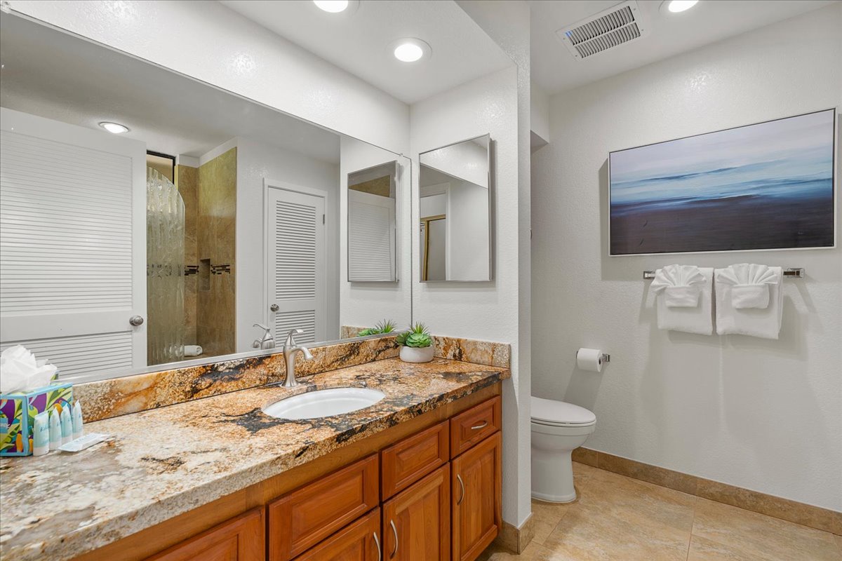 Freshen up in your private bathroom featuring a spacious granite vanity, walk-in shower, and thoughtful touches like fluffy towels and calming coastal artwork to enhance your stay.