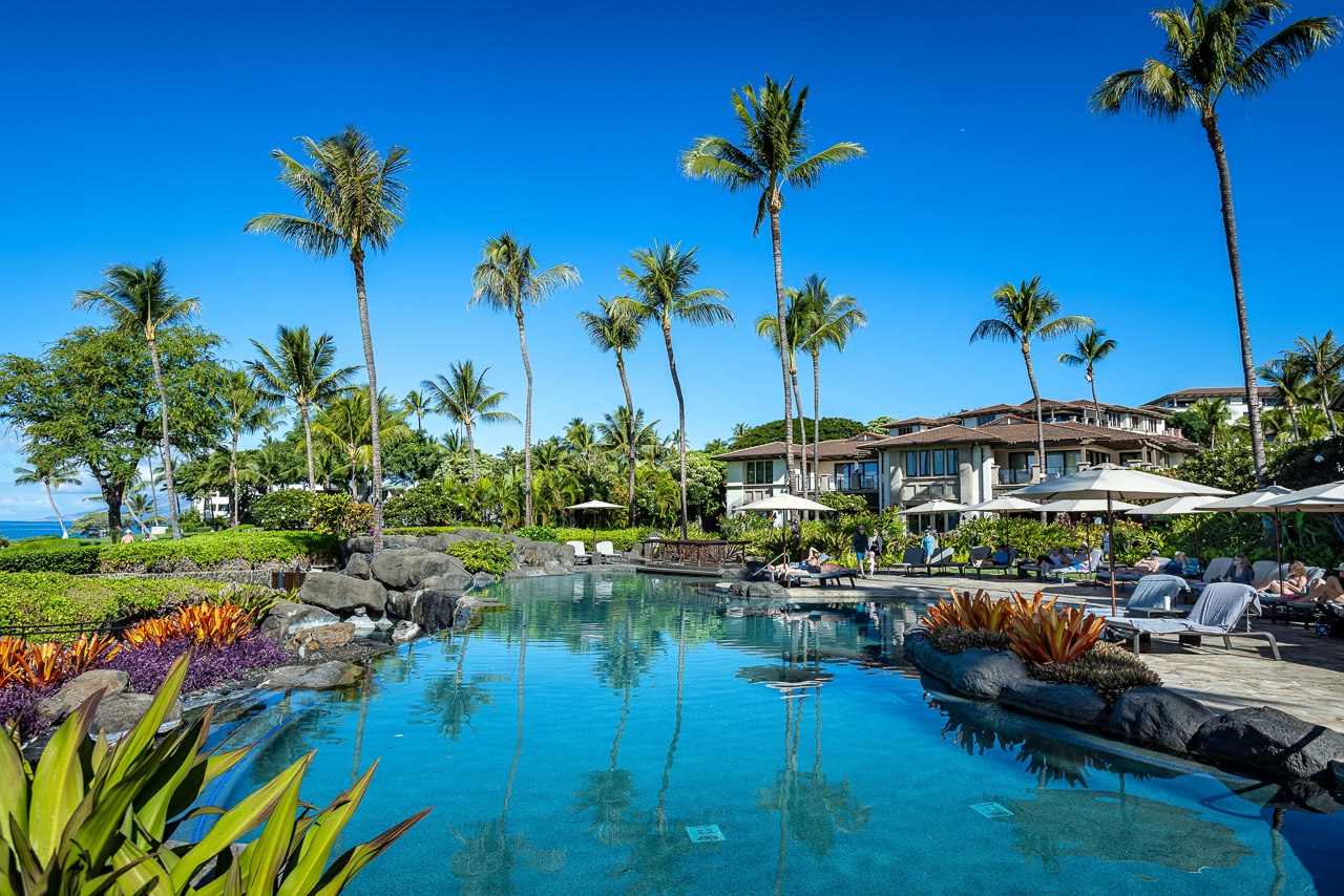 A stunning tropical pool surrounded by lush palms and volcanic rock, where crystal-clear waters invite you to relax under sunny Hawaiian skies.