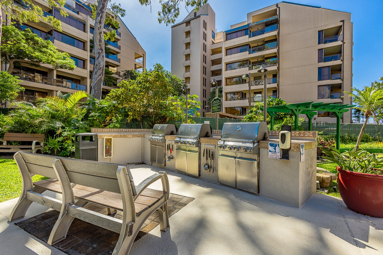 The property's outdoor BBQ area is surrounded by lush tropical landscaping and modern multi-story buildings, creating an inviting space for guests to gather and grill.