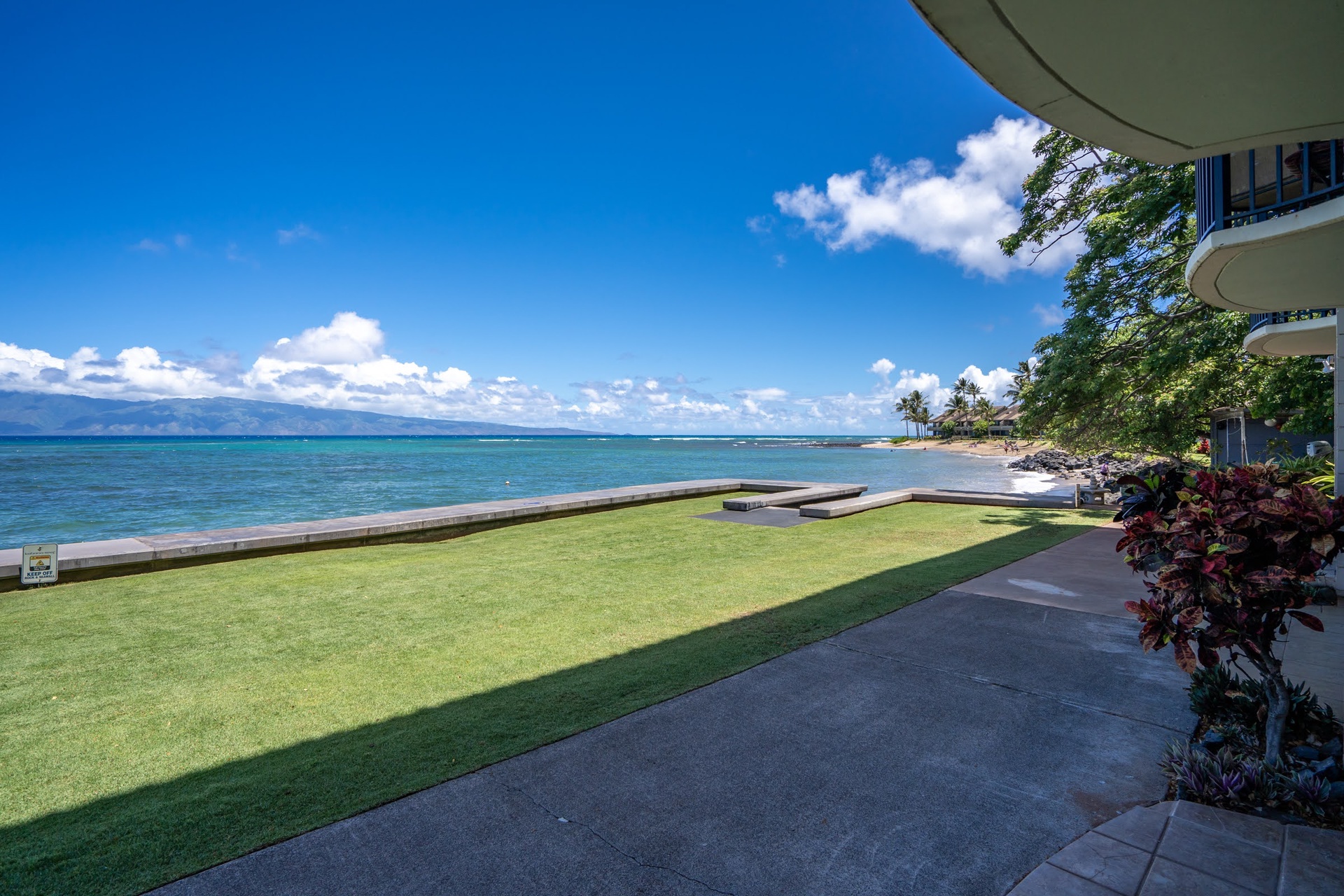 The property's manicured lawn extends right to the oceanfront, offering a stunning vantage point with turquoise waters, distant mountains, and a sweeping island horizon.