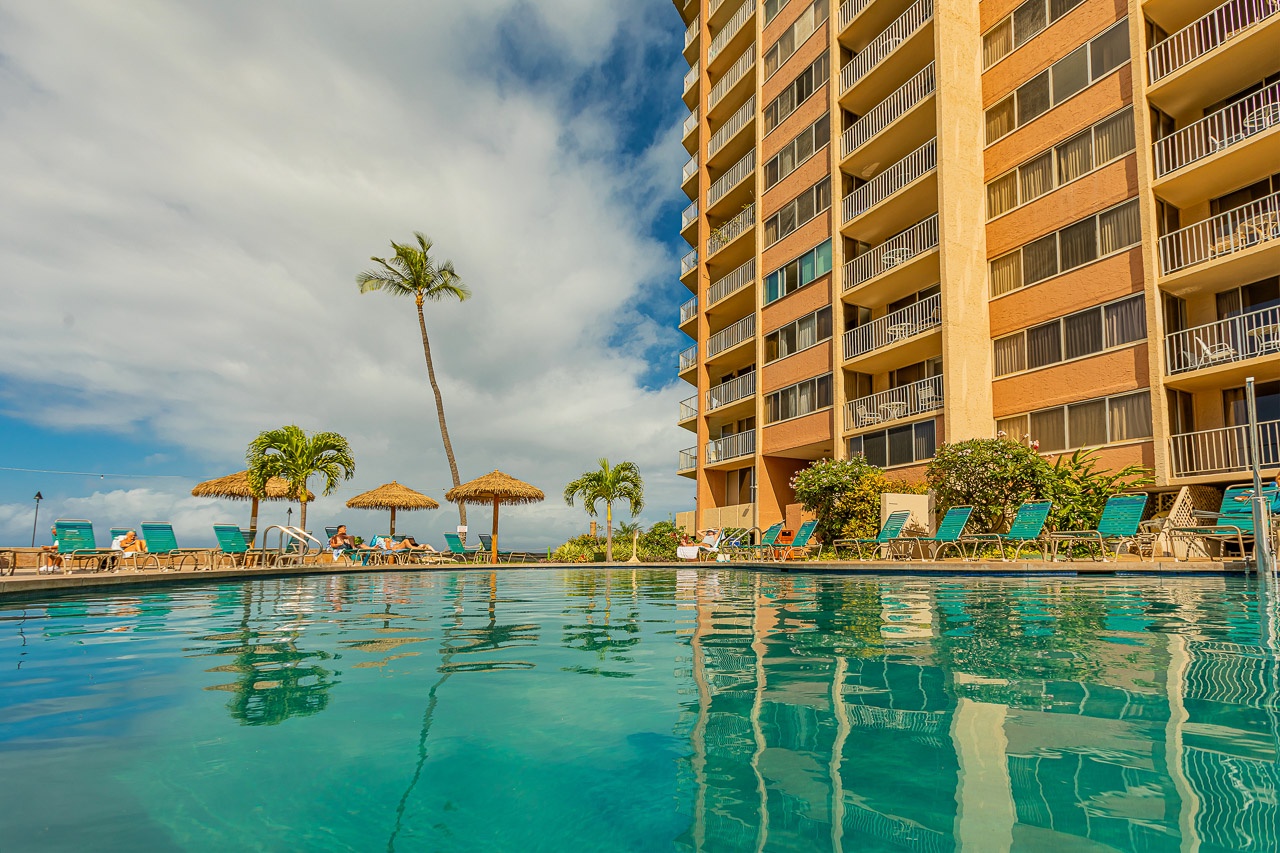 The beachside tower frames a sparkling pool where sunny days invite relaxation under swaying palms and thatched umbrellas.