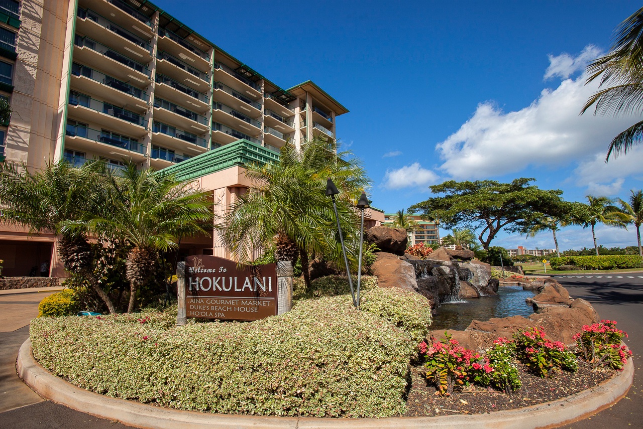 The Hokulani property welcomes guests with lush tropical landscaping, a cascading water feature, and stunning island surroundings under clear Hawaiian skies.
