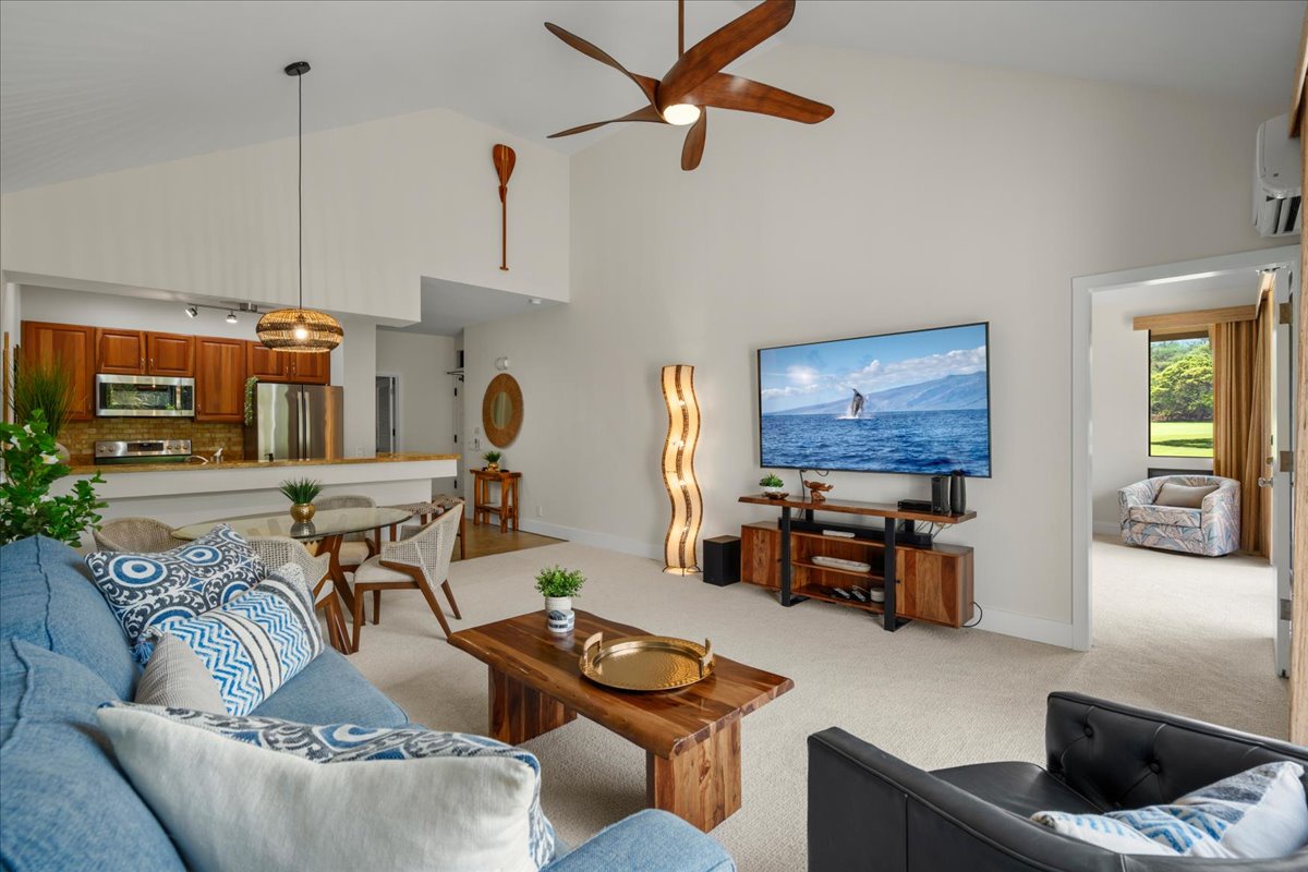 Relax in your bright, open-plan living area with a large TV, stylish furniture, and a fully-equipped kitchen. High ceilings and tropical decor invite you to unwind in comfort.
