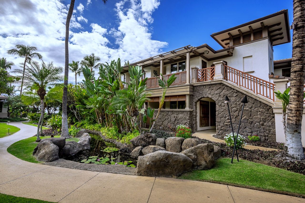 This tropical villa features distinctive stonework, dramatic outdoor stairways, and lush landscaping with palms, volcanic rock, and vibrant greenery, all set under serene island skies.