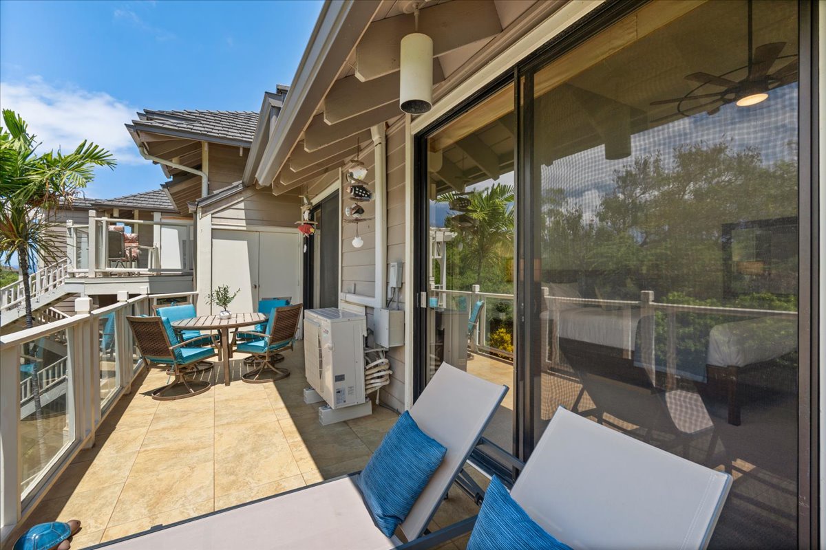 The covered balcony overlooks tropical scenery, offering a shaded spot to relax with refreshing breezes and vibrant turquoise accents that complement the sunny coastal atmosphere.
