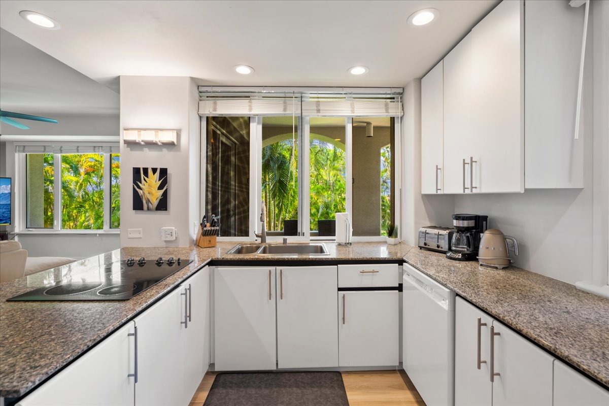 Step into your sleek, modern kitchen with bright white cabinetry and granite countertops, where every morning greets you with views of lush tropical greenery through expansive windows that bring the outdoors in.