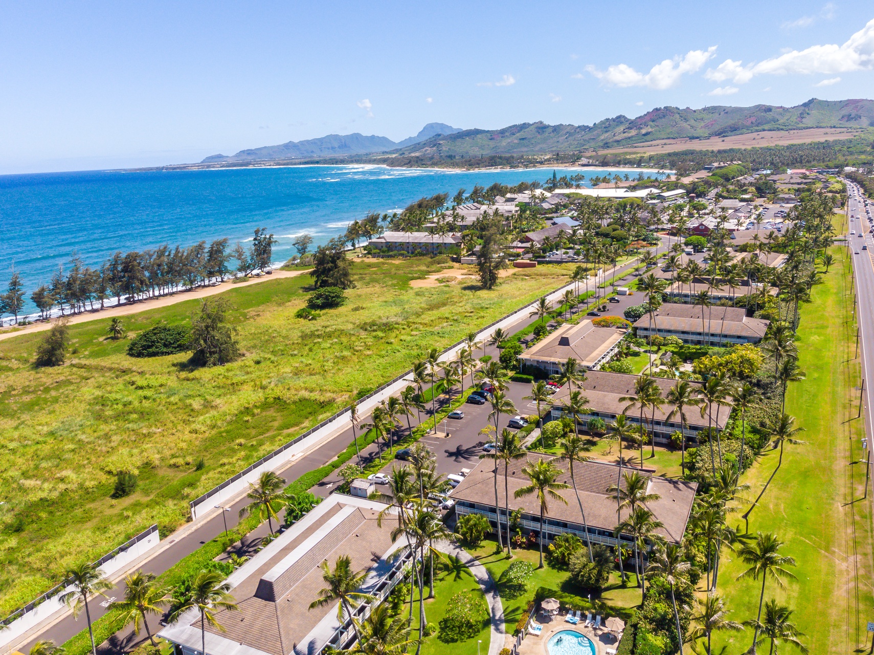 Stunning aerial view of beachfront property nestled between pristine coastline and lush mountains in tropical paradise.