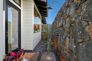 Private outdoor shower area surrounded by natural stone and tropical plants.