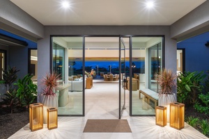 Step through elegant glass doors into your luxurious retreat, where warm lighting and tropical plants create an inviting welcome.