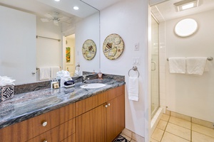 The bathroom in Papakea L-106 features a sleek granite vanity, accented by decorative wall pieces and soft lighting
