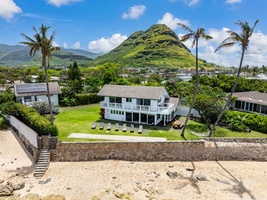 Your oceanfront vacation home with dramatic mountain backdrop and tropical palm trees creating an idyllic Hawaiian setting.