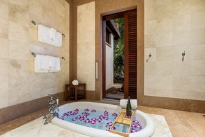 Sink into luxury in your private marble bathroom sanctuary, where purple petals float in warm water and tropical views await.