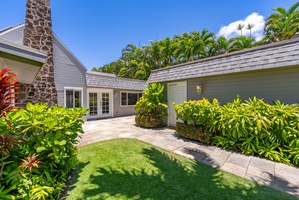 Charming property surrounded by lush tropical gardens under a brilliant blue sky, where a stone chimney and vibrant greenery create a serene island retreat.