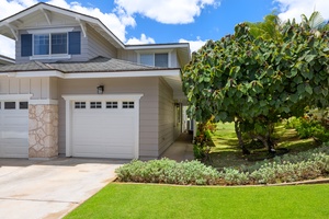 Modern two-story vacation home featuring covered garage parking and lush tropical landscaping with mature fruit trees and manicured lawn.