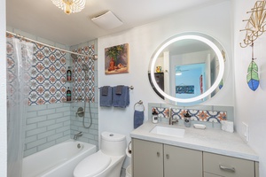 Full bathroom with shower/tub combo, colorful tile, and bright vanity lighting.