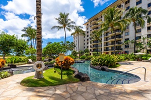 Resort pool area surrounded by lush tropical landscaping and palm trees under blue Hawaiian skies.