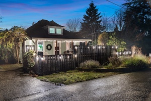 Enchanting holiday-lit property framed by lush greenery and a snowy winter sky.