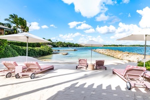 Plush beachfront loungers, shaded by umbrellas and set on pristine white sand with clear blue waters.