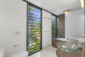 An elegant ensuite with floor-to-ceiling louvered windows and tropical views.