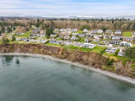 Aerial view of waterfront residential community with homes along the shoreline, surrounded by forests and distant mountains.
