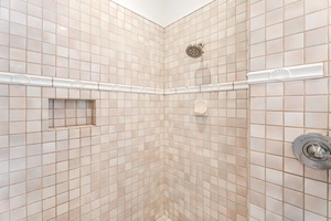 Neutral-toned walk-in shower with built-in shelves, blending convenience with clean, tropical-inspired tilework.