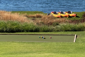 Seaside bocce lane with kayaks and calm blue water beyond.